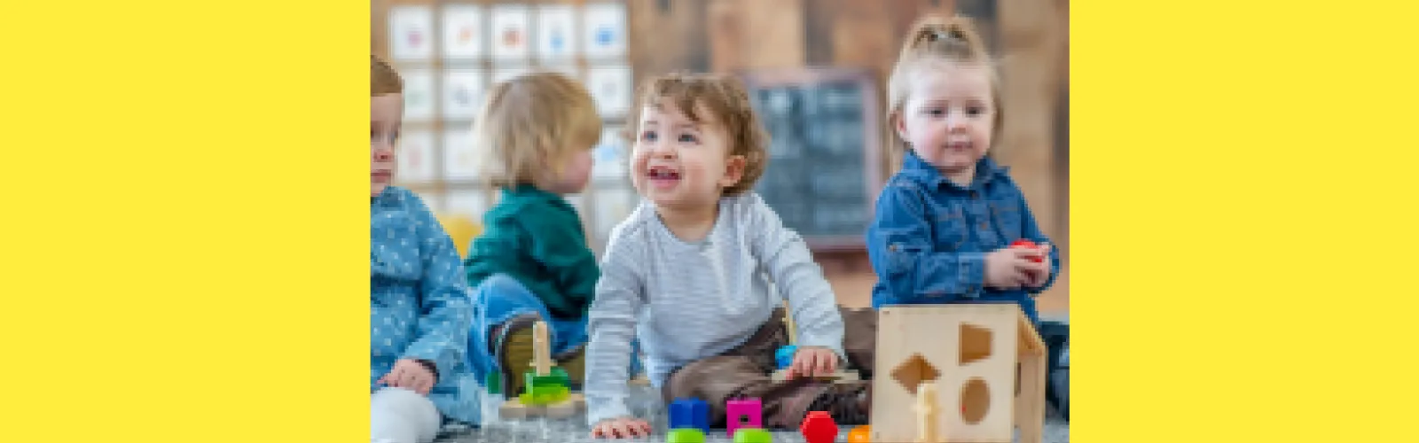 Three toddlers playing with toys in front of a window with a yellow background