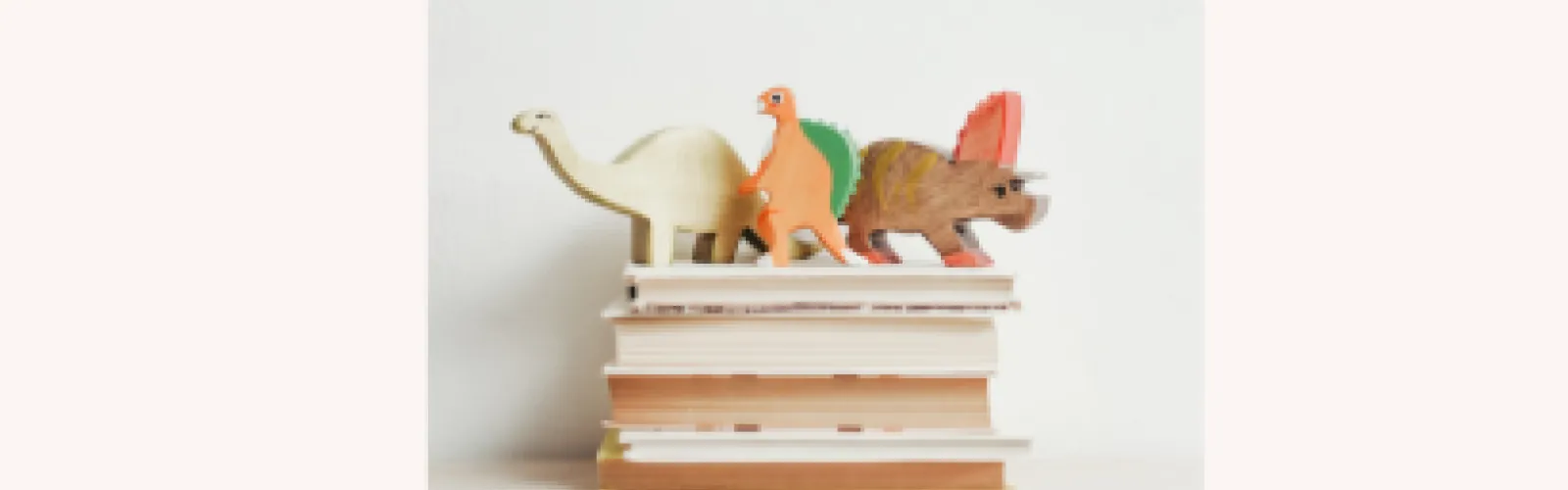 Three wooden dinosaurs on a stack of books