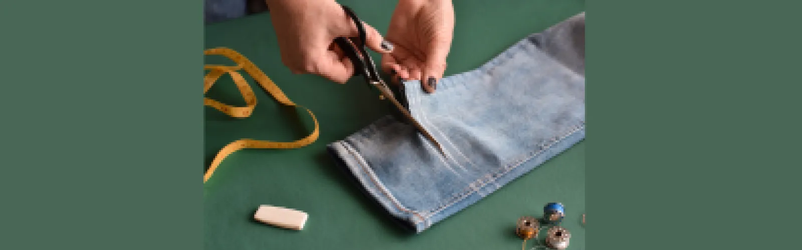 The leg of a pair of jeans that has the hem cut and marked and some sewing supplies