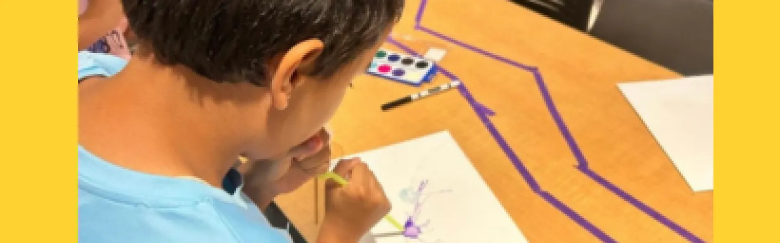 Boy blowing paint with paint through the straw on white piece of paper 