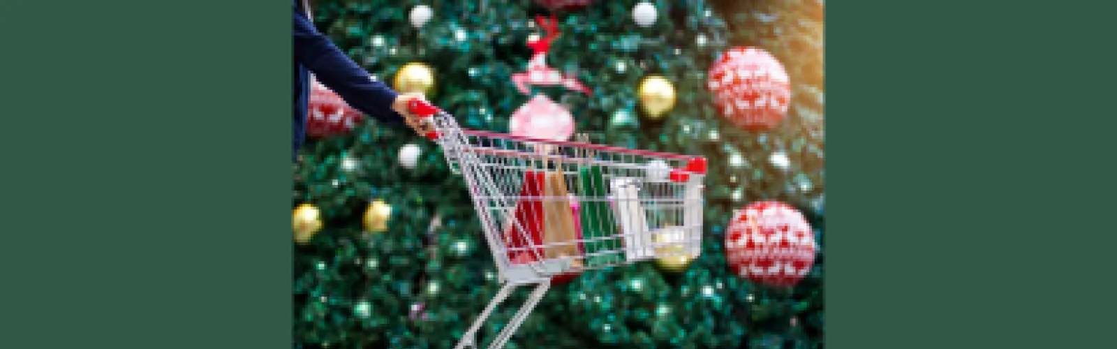 A shopping basket with items in it in the foreground and a Christmas tree in the background
