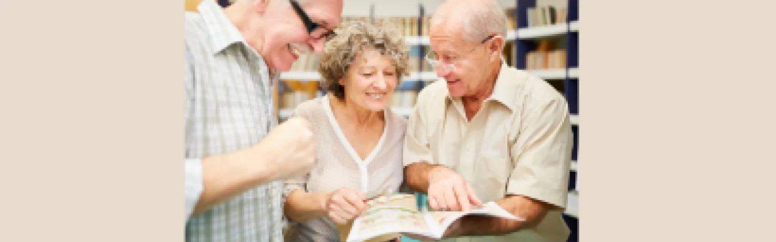 Three older adults looking at a book and smiling with beige background