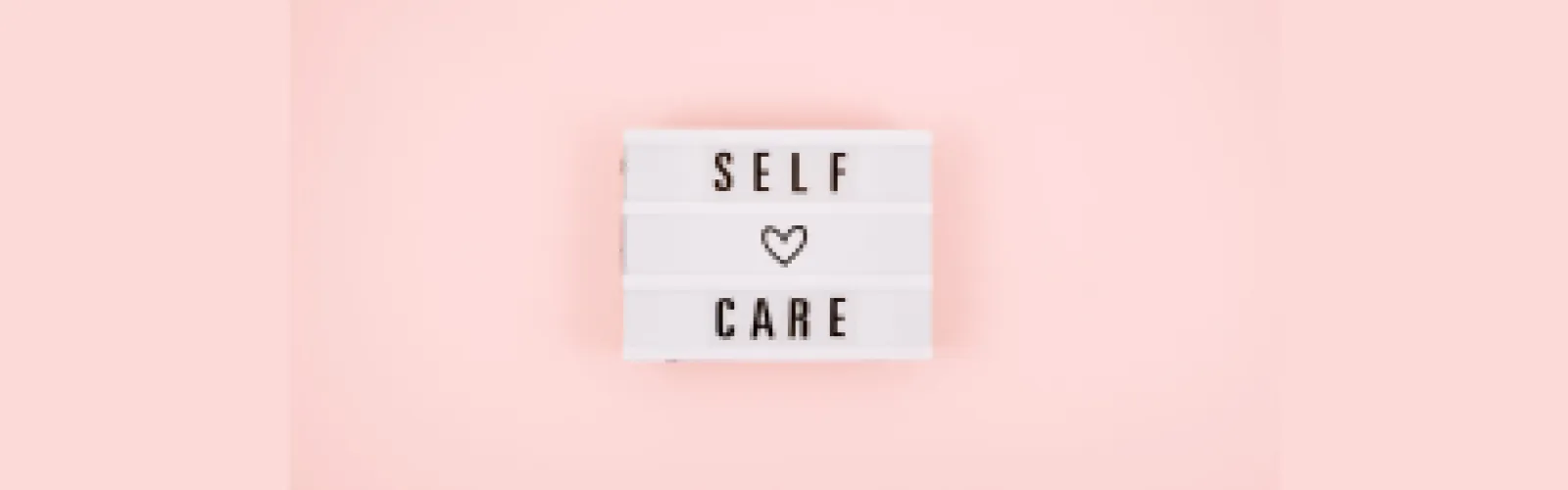Self Care on Sign with heart between the words with a pink background