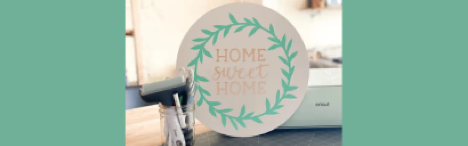 Home Sweet Home round wooden sign with green border next to tools and Cricut machine on green background