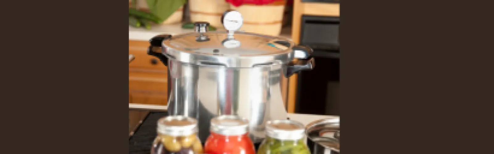 Canning pot with gauge and canned vegetables in the foreground on a dark background