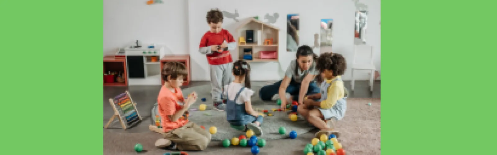 Kids playing in a group with one adult with toys scattered around them on a green background