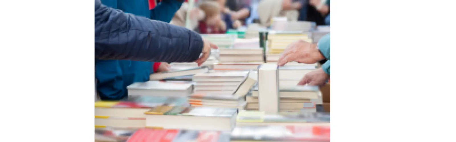 Books arranged on a table and hands sorting through the stacks