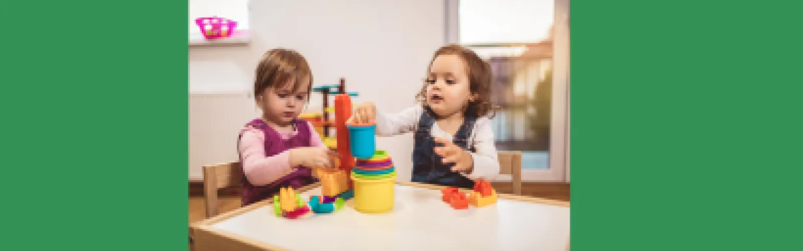 Two toddlers building towers of blocks on a table